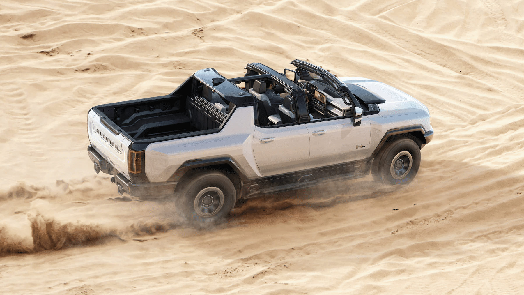 A silver 2023 Hummer EV Pickup drives through sand dunes